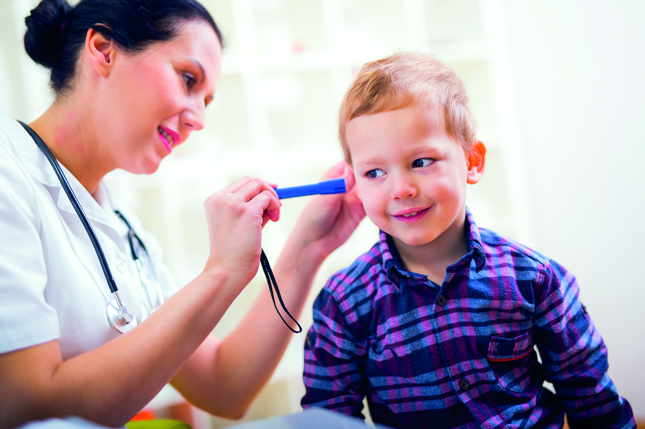 Eine Ärztin leuchtet in das Ohr eines Jungen und prüft dessen Ohrhygiene