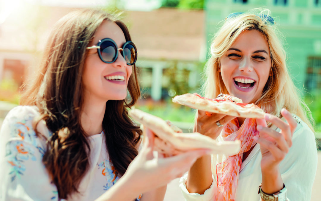 Zwei lachende junge Frauen essen Pizza – abnehmen mit Genuss.