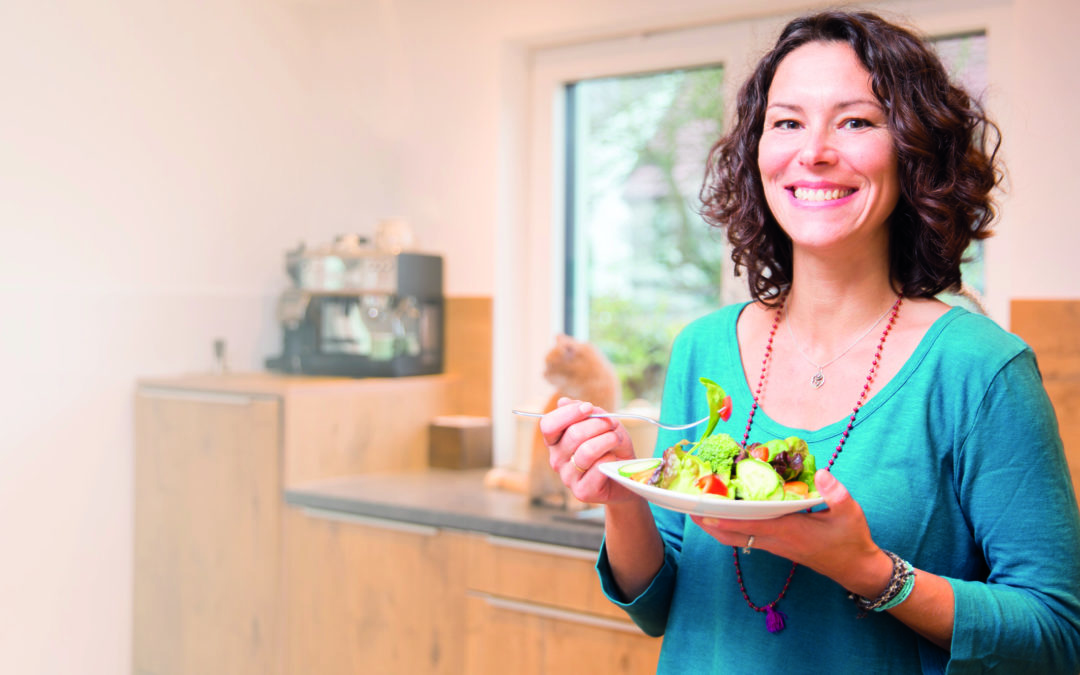 Frau in der Küche isst gesundes Gemüse und lächelt in die Kamera (Die Schilddrüse)