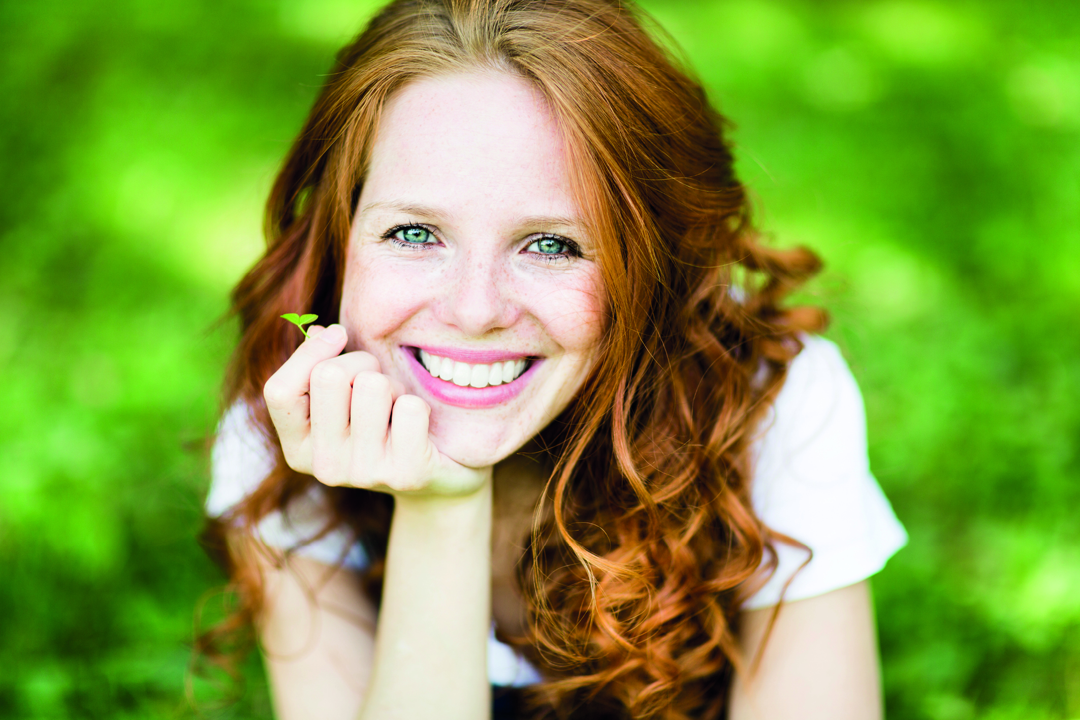 Rothaarige Frau mit strahlendem Lächeln vor grünem Hintergrund. (Erste Hilfe für Zähne)