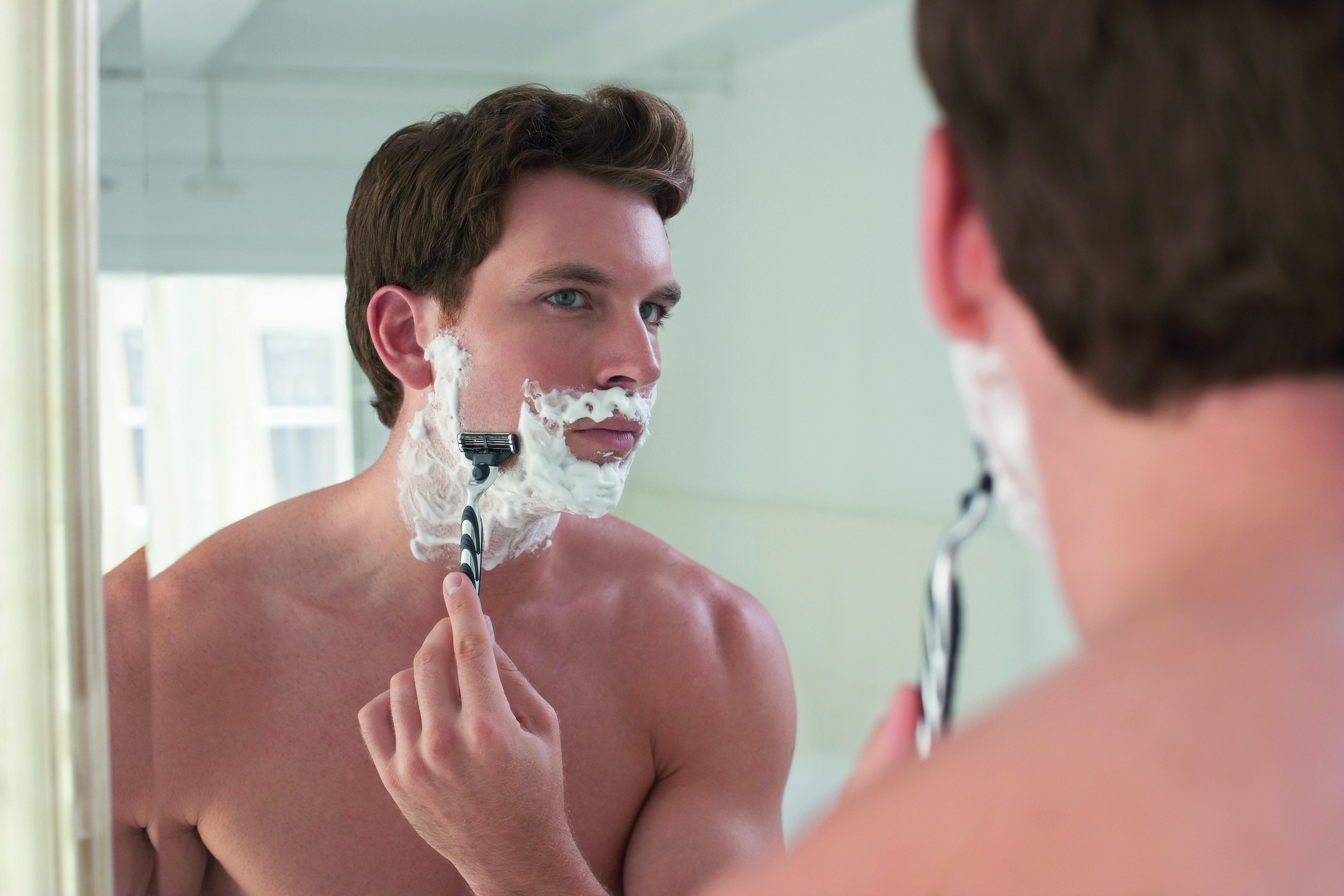 Tägliche Pflege: Ein Mann steht vor dem Spiegel und rasiert sein Gesicht