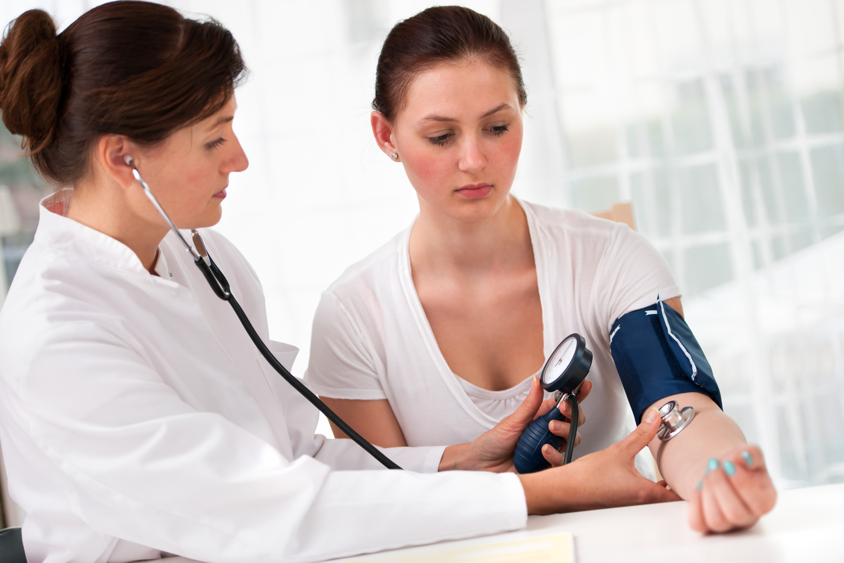 Eine Ärztin misst den Blutdruck einer jungen Frau.