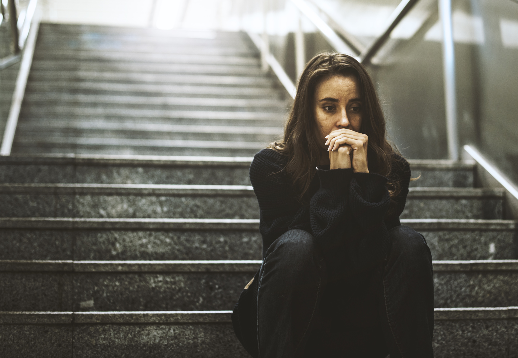 eine depressive Frau sitzt im Schatten auf einer dunklen Steintreppe.