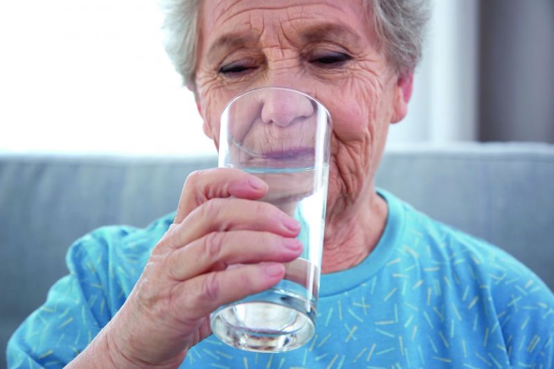 Eine ältere Frau trinkt aus einem großen Glas.