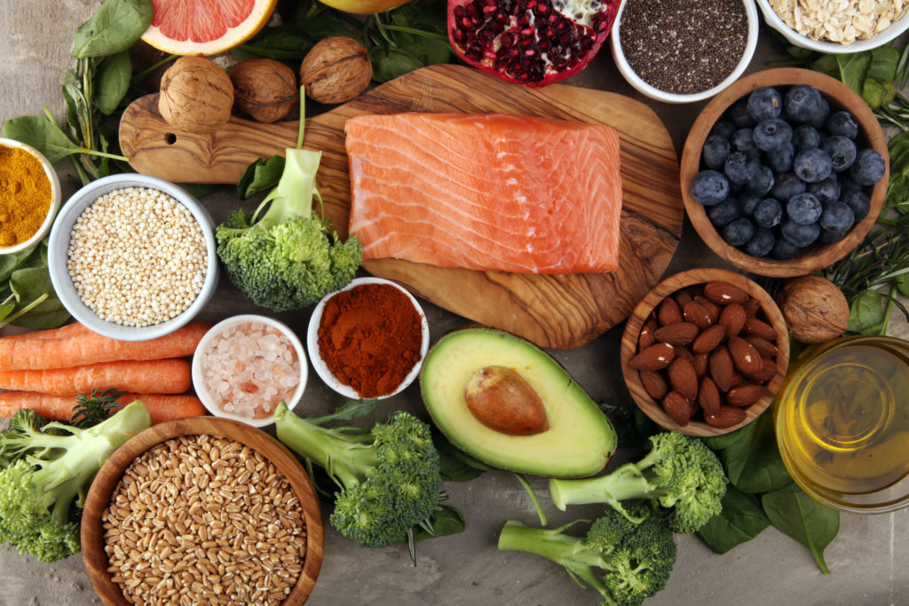Immunsystem stärken: Fisch, buntes Gemüse und Obst, Nüsse, Gewürze, Kräuter und Öle nebeneinander