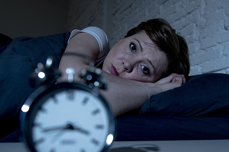 Laute Nachbarn: eine Frau liegt schlaflos im Bett und schaut ihren Wecker an.
