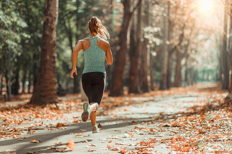 Eine Frau joggt in einem Waldstück bei Sonnenschein (laute Nachbarn).