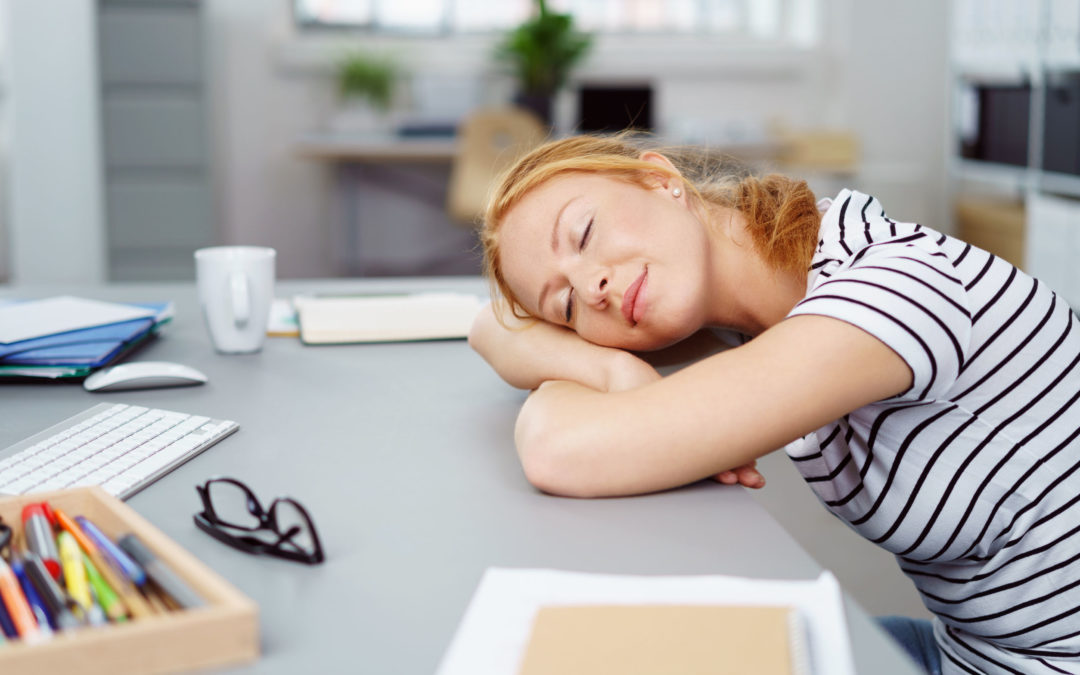 Powernapping: eine junge Frau liegt mit dem Kopf auf dem Schreibtisch und schläft.